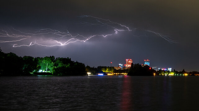 View of a powerful lightning bolt illuminating the night sky over the city skyline and lake in Bucharest, Bucharest, Romania.