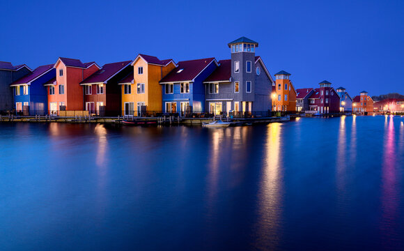 View of colorful houses along the Reitdiephaven canal at twilight with reflections on the water surface in the Netherlands.