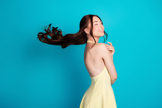 Joyful young woman in a backless yellow dress with flowing hair captured mid-twirl against a bright turquoise background &mdash; carefree portrait of motion, summer style and natural beauty