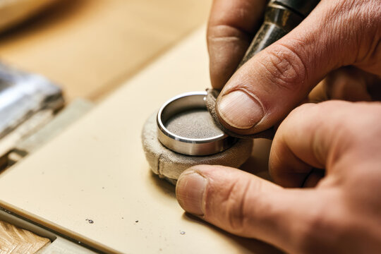 A skilled craftsman is carefully shaping a metal ring on a work surface, illustrating dedication, craftsmanship, and the artistry involved in creating handmade jewelry.