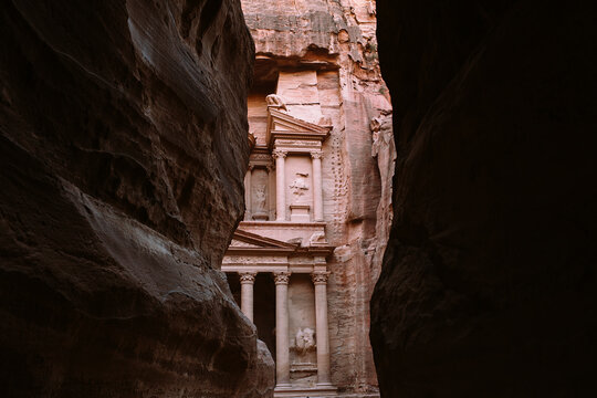 First glimpse of Al-Khazneh temple framed by the dark walls of the Siq gorge in Petra. Ancient Nabataean treasury architecture.