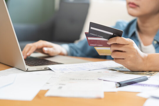 Stressed Asian young woman holding credit cards while using laptop to check online bills, feeling worried about monthly expenses, debt and financial crisis at home.
