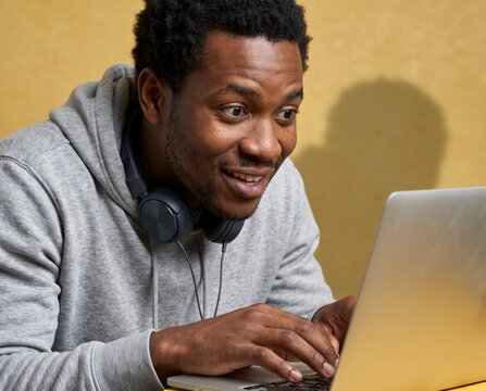 Engaged freelancer wearing headphones typing on silver laptop against warm yellow wall
