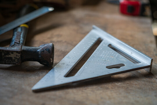 View of a metal speed square and a claw hammer resting on a wooden workbench in a workshop in Looe, Cornwall, United Kingdom.