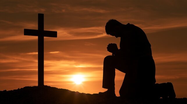 Silhouette of a man kneeling in prayer before a wooden cross at sunset