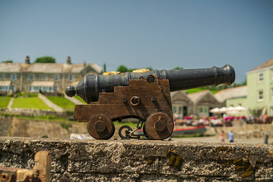 View of an antique cannon on a wooden carriage resting on a stone wall in the historic harbor village of Charlestown, Cornwall, United Kingdom.