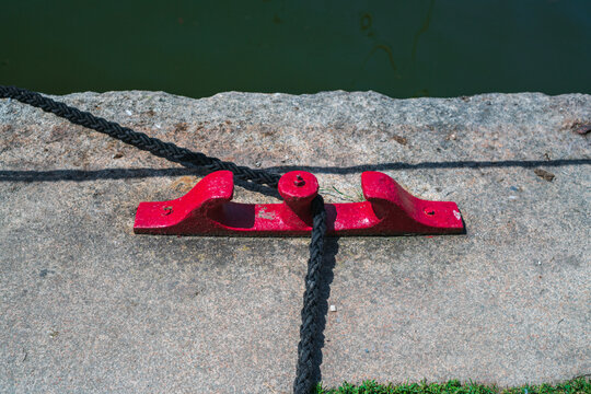 View of a red metal mooring cleat with a black rope on a stone quay in Charlestown, Cornwall, United Kingdom.