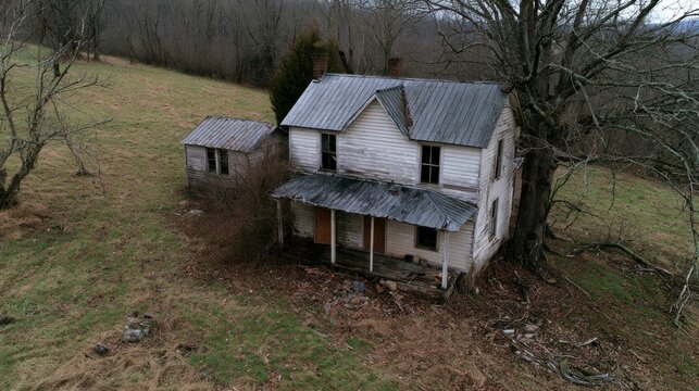 Aerial view of a dilapidated and abandoned two-story farmhouse with a small outbuilding in a rural winter landscape
