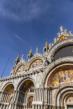 Venice, Veneto, Italy - 21 September 2026: View of the ornate facade of St. Mark's Basilica featuring intricate mosaics, marble columns, and golden statues under a clear blue sky.