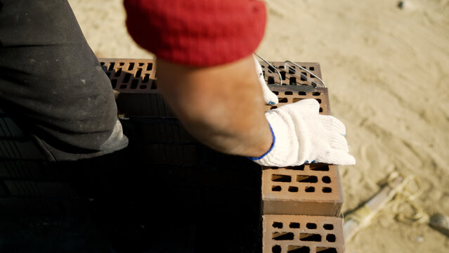 Red shirt and white glove of bricklayer building wall with perforated clay bricks and wire mesh, house construction