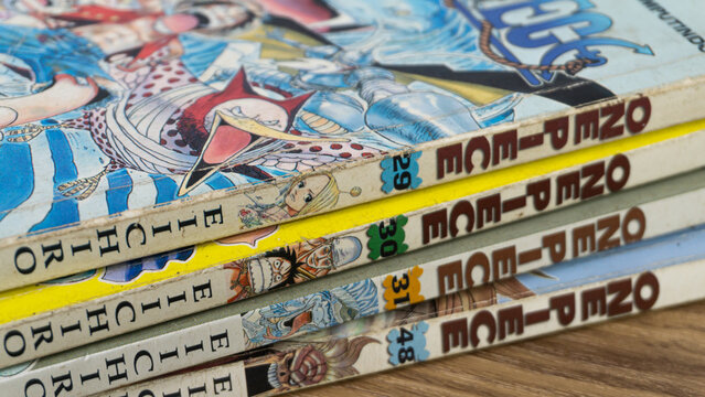 SOUTH KALIMANTAN, INDONESIA - SEPTEMBER 30, 2026: An angled close view displays four One Piece comic books authored by Eiichiro Oda lying stacked horizontally on a brown wood table.