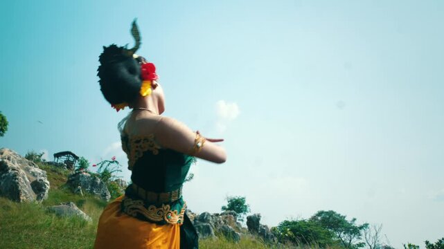 A powerful side view of a dancer in traditional costume performing a martial arts-inspired dance move (silat style) against a blue sky.