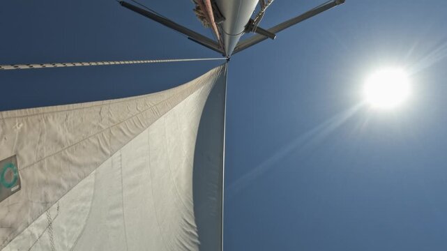 Sailboat mast and white sail under the sun on a clear day