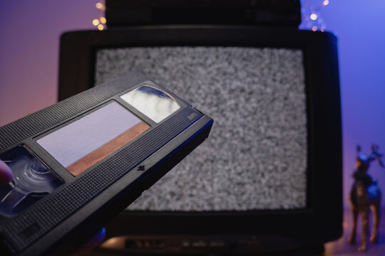 Hand holding VHS tape in front of old television static screen