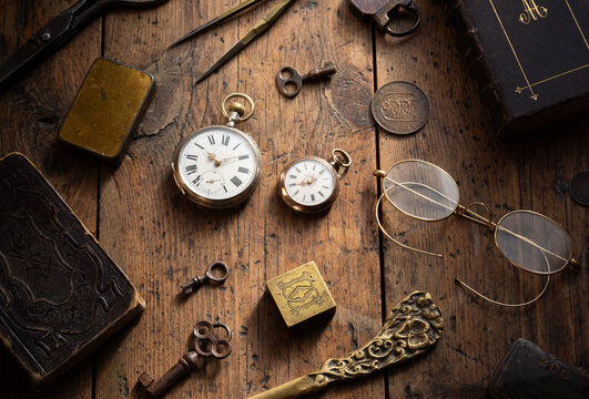 Vintage collection of antique objects arranged on an old wooden table, including pocket watches, keys, coins, books. Rustic still life evoking history, antique, atmosphere of a Victorian study.