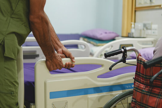 Healthcare worker assisting a man in a hospital room beside a wheelchair, showing patient care, medical support and assistance with mobility during treatment and recovery.
