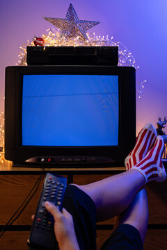 Person using remote control while relaxing in front of retro CRT television with Christmas decorations