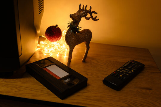 VHS videocassette and remote control beside glitter reindeer and warm Christmas lights