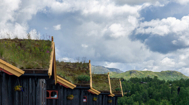 Traditional cabins featuring grass and moss sod roofs blend into the mountainous Scandinavian landscape, showing sustainable architecture and natural beauty under a cloudy sky