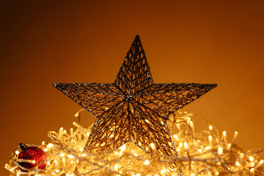 Glitter Christmas star decoration surrounded by warm fairy lights and red ornament, festive holiday background with golden glow