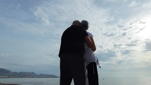 Pareja madura abrazada contemplando el mar desde la playa