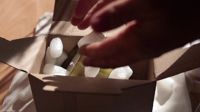 Pouring white biodegradable starch filler into a cardboard box with a glass candle for eco packaging of parcels. Box is filled with a filler safe for the environment that dissolves in water. 
