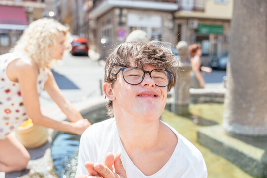 Cheerful teenage boy with Down syndrome making funny face outdoors on sunny summer day