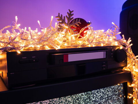 Vintage VHS player with videocassette surrounded by Christmas lights and holiday decorations, retro home video technology concept