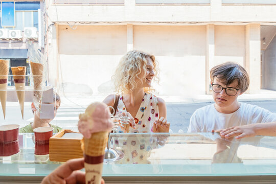 Ice cream seller serves a fresh scoop of pink artisanal gelato in a waffle cone while customers wait at the counter in a local Spanish shop.