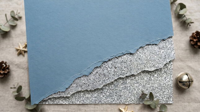 Torn paper layers in blue and silver tones rest on a neutral surface surrounded by pinecones and seasonal accents.
