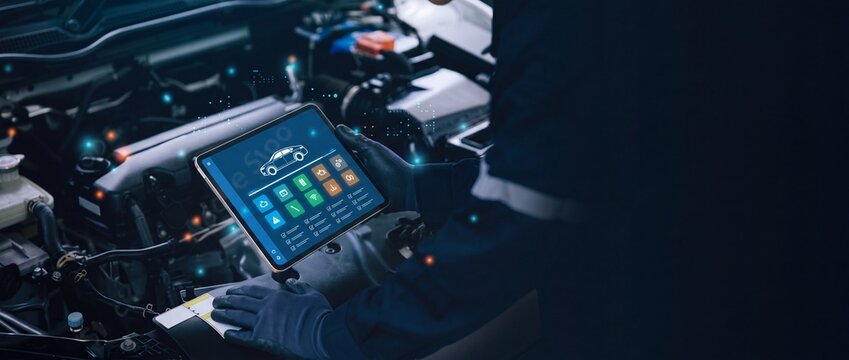 Professional auto mechanic using a digital tablet for vehicle engine diagnostics and maintenance in a modern workshop, showing high-tech smart car repair and automotive diagnostic software