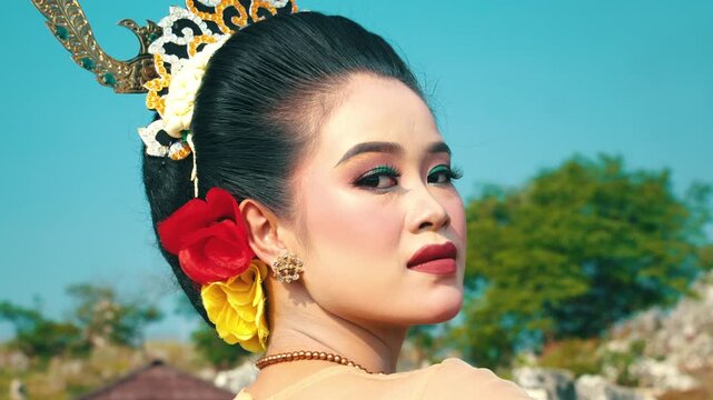 A stunning close-up portrait of a traditional dancer's face with heavy stage makeup and a confident expression, looking back at the viewer over her shoulder.