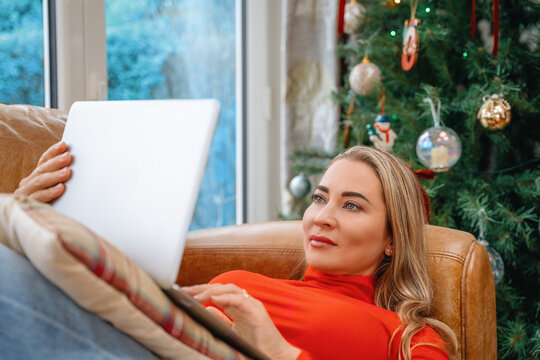 Woman using laptop on a couch next to a Christmas tree in a cozy room