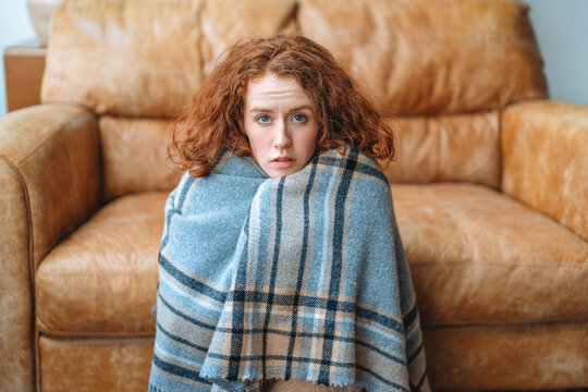 Woman sitting on a couch wrapped in a blanket while looking at the