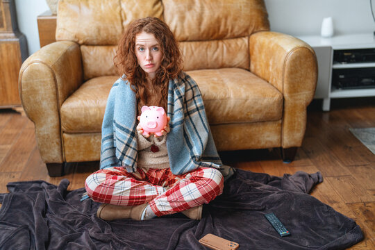 Person sitting on a blanket holding a piggy bank in a living room