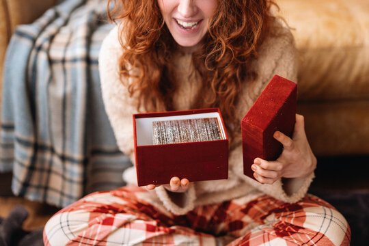 Woman opening a red gift box while sitting on the floor at home in
