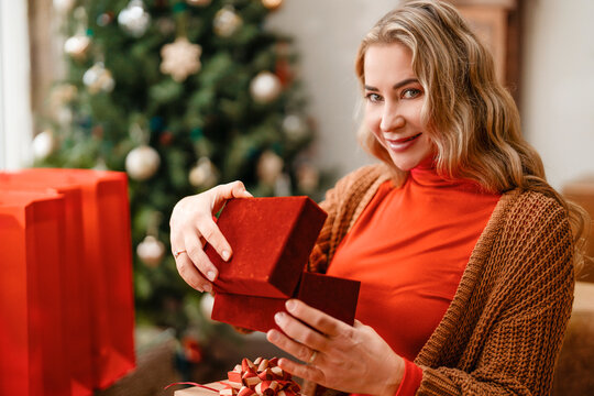 A woman sits at a table smiling while she opens a gift