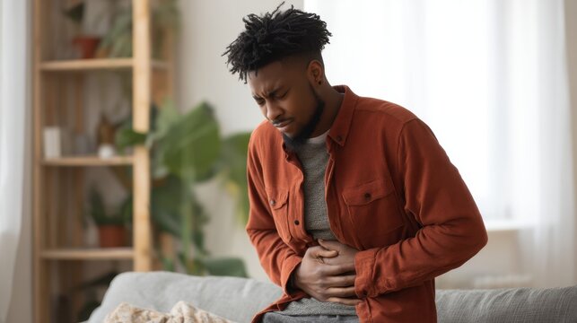 Stressed African Man Feeling Unwell with Abdominal Discomfort Standing Near Window Indoor
