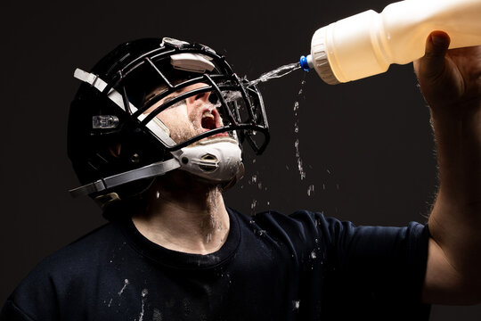 American Football Player in Helmet Drinking Water with Water Spl