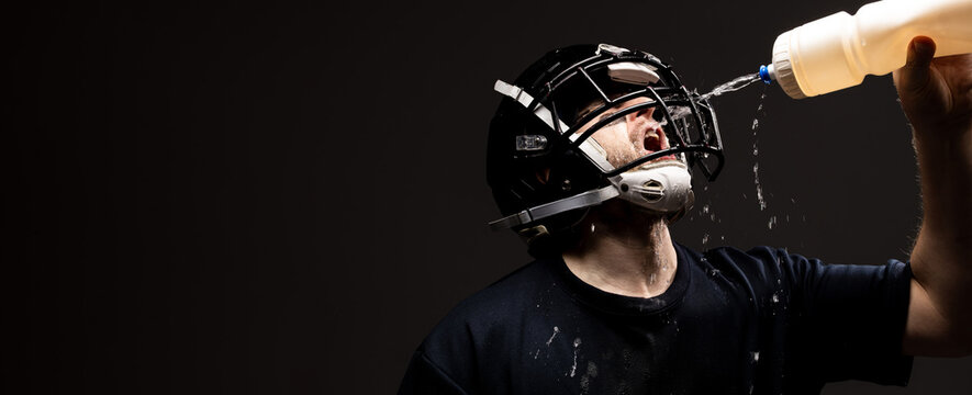 American Football Player in Helmet Drinking Water with Water Spl