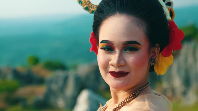 A captivating headshot of a female dancer with elaborate traditional makeup and hair accessories, smiling warmly and directly at the camera.
