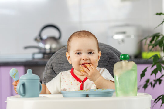 Messy baby girl eating finger food happily in high chair