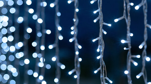 Clusters of white glowing holiday lights hanging in parallel vertical strands against a deep navy night sky, soft diffuse bokeh halos around each bulb, gentle warm-white glow, fest