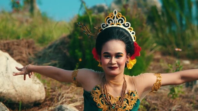 A joyful shot of an Indonesian dancer spreading her arms wide open with a beaming smile, celebrating cultural heritage in a natural limestone setting.