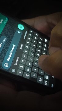 Close-up of hands typing a message on a smartphone using a virtual keyboard at night, texting on a mobile phone messaging app