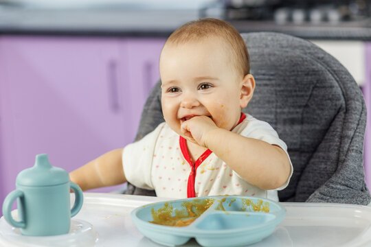 Laughing baby eating finger food with messy face in high chair