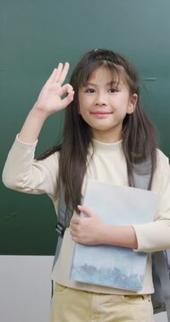 Playful student girl making OK sign with hand over her eye and smiling cheerfully.