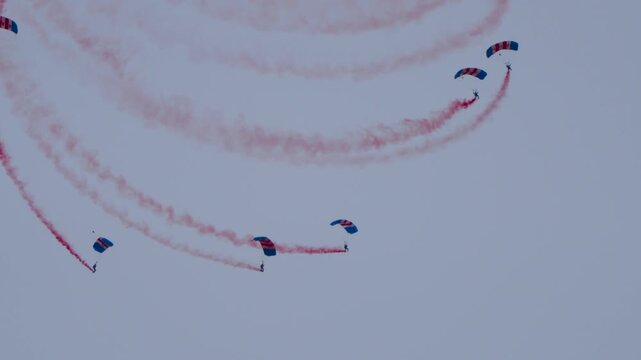 Parachute team floating in the sky with red smoke trails