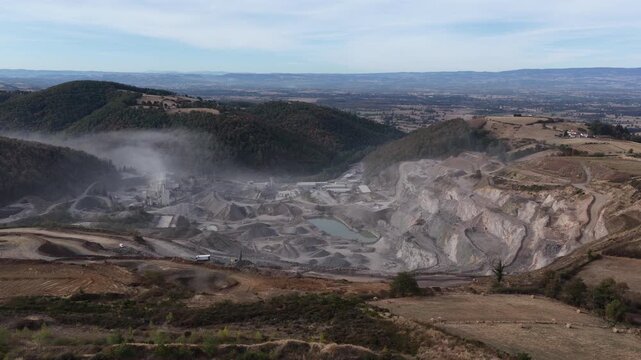 Wide aerial open-pit quarry processing plant and dusty hillsides