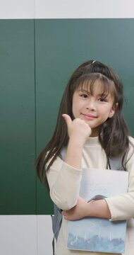 Cute student girl holding books and giving a thumbs up gesture with a confident smile.
